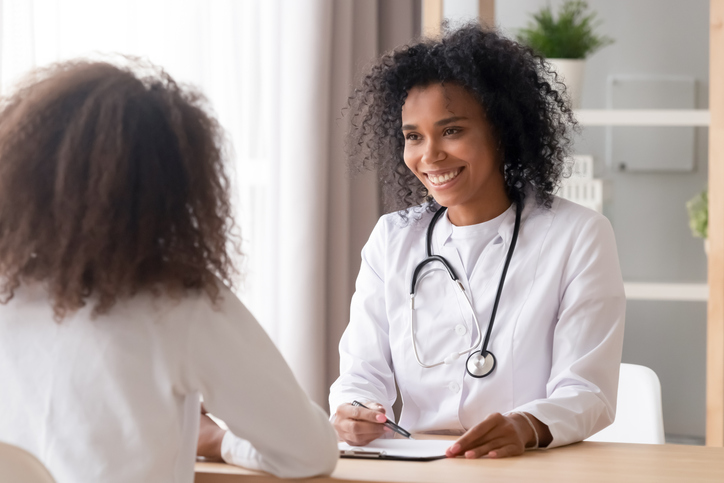 Smiling african female doctor talking to teen patient making notes