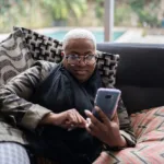 woman laying on her couch, looking at a menopause app on her smartphone