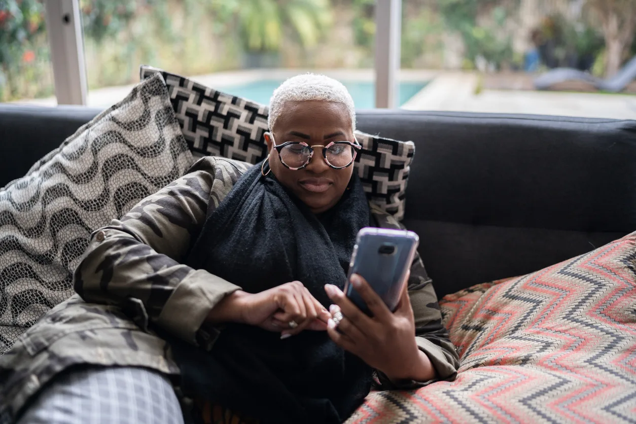 woman laying on her couch, looking at a menopause app on her smartphone