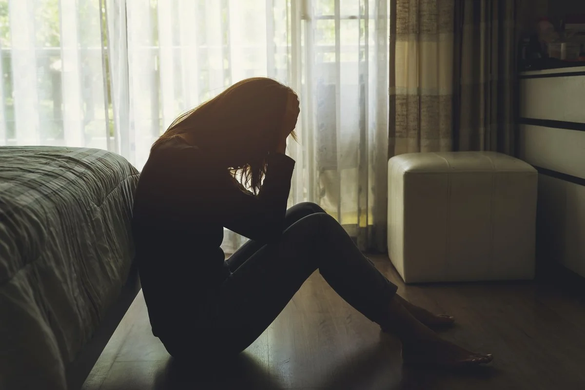 woman sitting at the end of her bed with her head in her hands