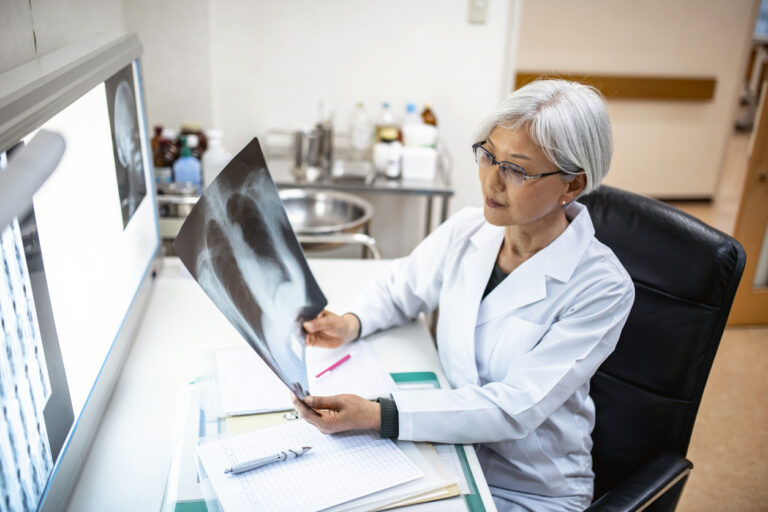 Female Japanese doctor seated in her office and examining x-ray imagery before deciding on a diagnosis.