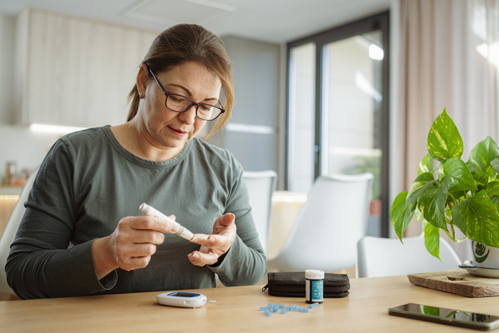 Mature diabetic woman using lancet on finger for checking blood sugar level by Glucose meter